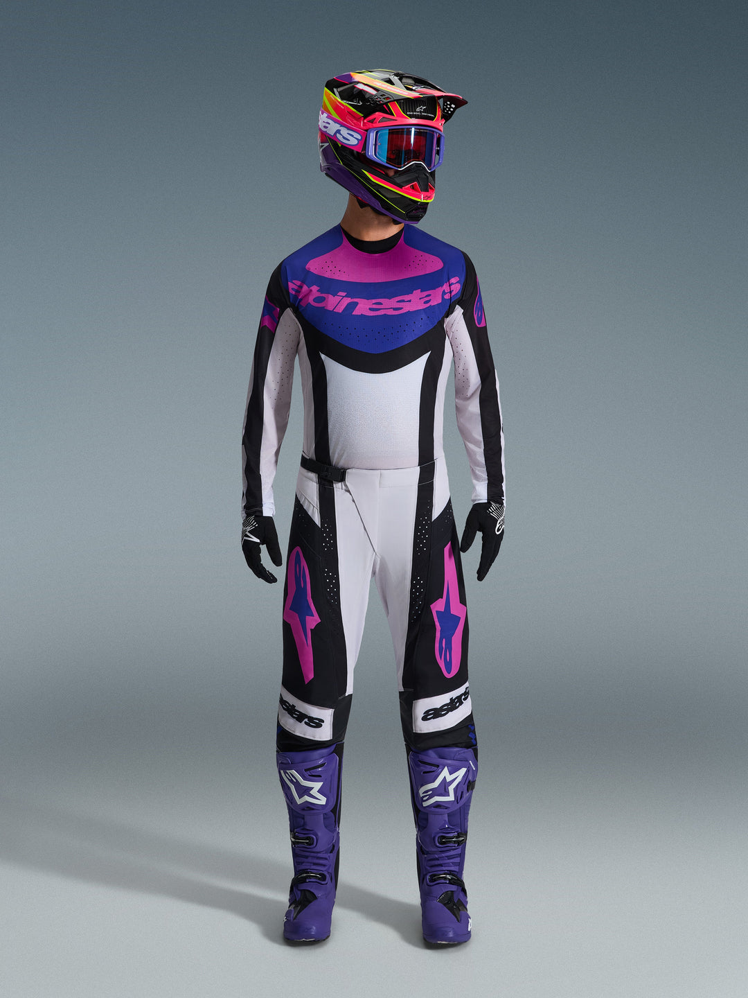 Alpinestars 2026 Techstar Knif Gear Set, equipamento completo de motocross, branco, preto, roxo e rosa, usado com um capacete multicolorido, óculos azuis, botas roxas e luvas pretas, conjunto de alta performance coordenado para corridas de todo-o-terreno