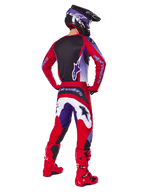 Piloto de motocross visto de costas a usar calças Alpinestars 2025 Fluid Wurx, roxo e vermelho vivo com pormenores em branco e preto, camisola a condizer, capacete preto e botas vermelhas, conjunto coordenado para corridas de todo-o-terreno