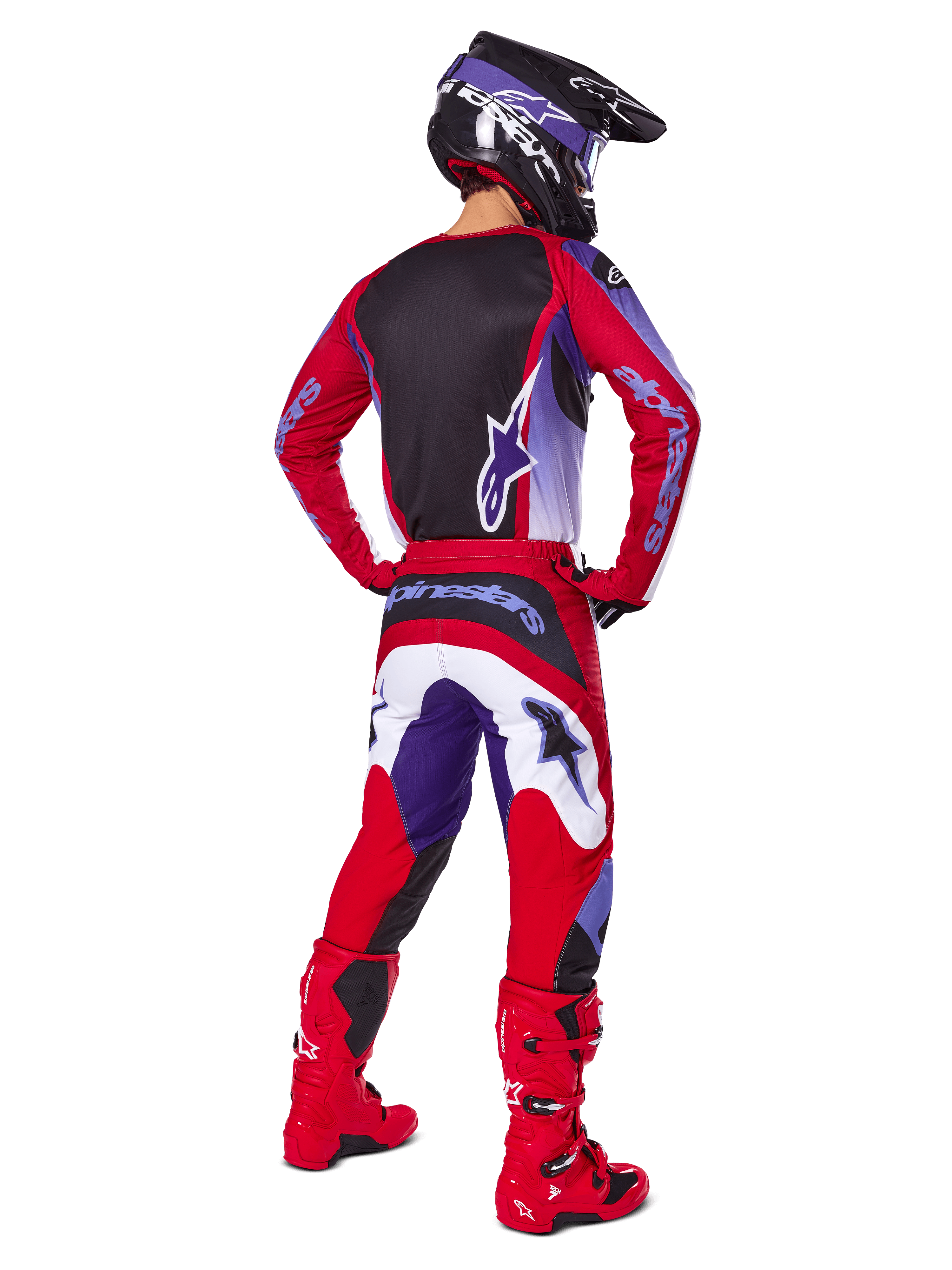 Piloto de motocross visto de costas a usar calças Alpinestars 2025 Fluid Wurx, roxo e vermelho vivo com pormenores em branco e preto, camisola a condizer, capacete preto e botas vermelhas, conjunto coordenado para corridas de todo-o-terreno