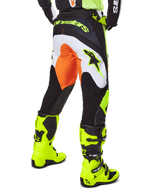 Alpinestars 2025 Fluid Wurx Pants, calças de motocross, amarelas e pretas com detalhes em laranja e branco, vista traseira, usadas com botas amarelas vibrantes a condizer, construção durável com logótipos em destaque para a prática de motocross