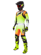Piloto de motocross a usar as calças Alpinestars 2025 Fluid Wurx em amarelo e preto, com um gradiente vibrante de amarelo para branco e detalhes em laranja e preto, apresentadas como parte de um conjunto completo de equipamento de corrida com camisola a condizer, capacete preto e botas amarelo néon.