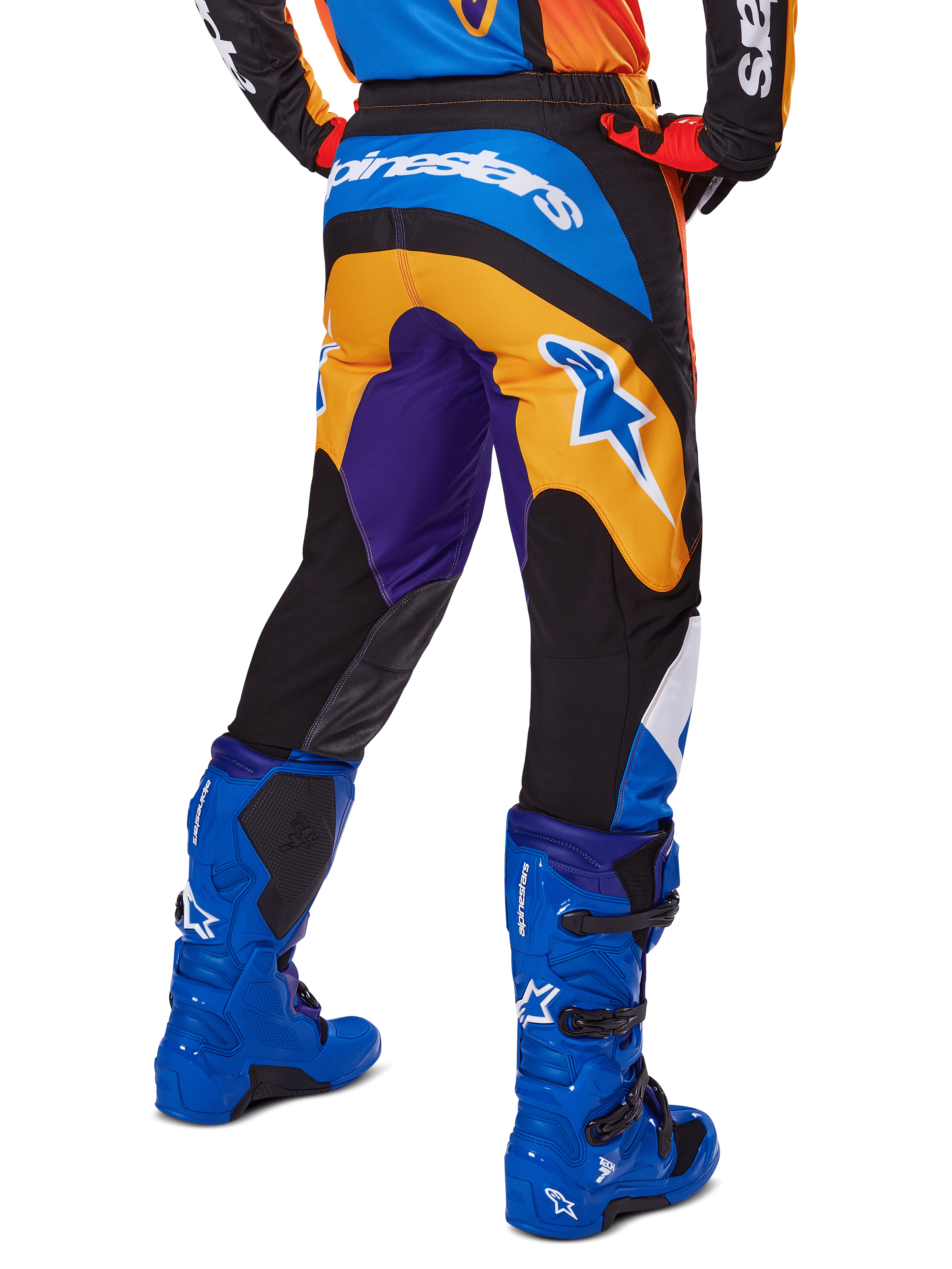 Alpinestars 2025 Fluid Wurx Pants, calças de motocross, multicor com laranja, roxo e azul, vista traseira mostrando o logótipo Alpinestars branco na parte de trás, combinadas com botas de motocross azuis, ajuste atlético para corridas todo-o-terreno