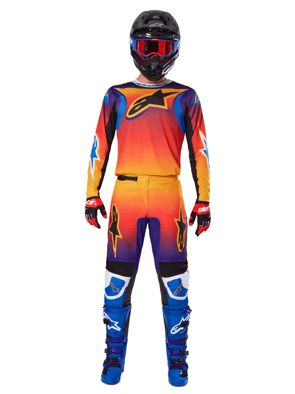Calças Alpinestars Fluid Wurx 2025, calças de motocross, gradiente multicolorido de laranja, amarelo e roxo, usadas com camisola a condizer, capacete preto com óculos azuis, luvas vermelhas e pretas, e botas azuis, equipamento de motocross coordenado