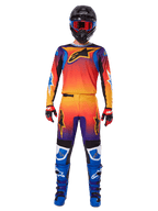 Calças Alpinestars Fluid Wurx 2025, calças de motocross, gradiente multicolorido de laranja, amarelo e roxo, usadas com camisola a condizer, capacete preto com óculos azuis, luvas vermelhas e pretas, e botas azuis, equipamento de motocross coordenado