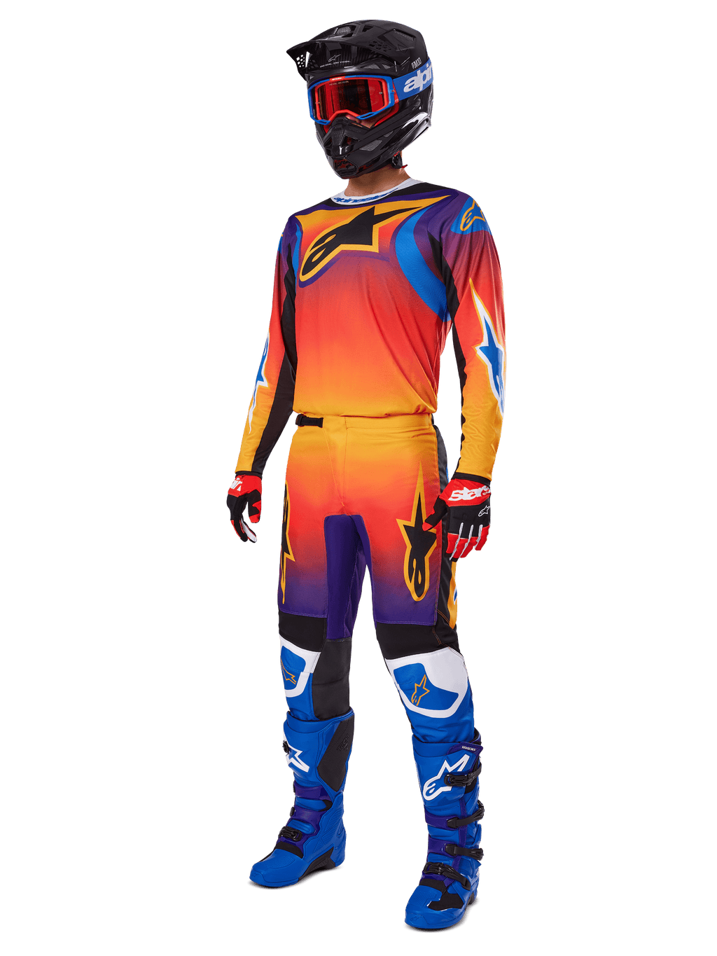 Piloto de motocross com equipamento de corrida completo, calças Alpinestars 2025 Fluid Wurx e camisola a condizer com gradiente multicolorido em laranja, vermelho e roxo, capacete preto com óculos vermelhos, botas azuis e pretas e luvas vermelhas e pretas; conjunto coordenado para todo-o-terreno