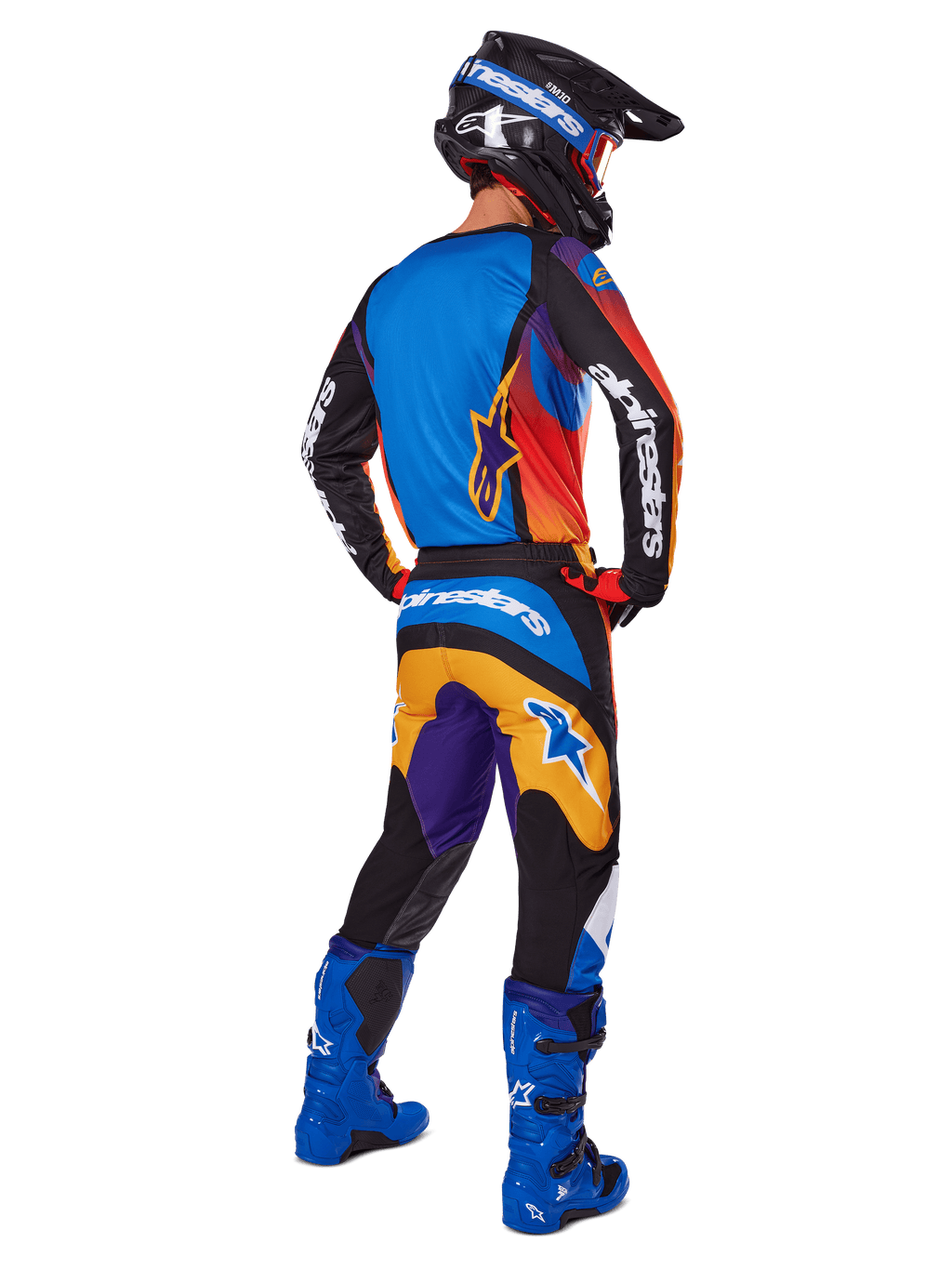 Piloto de motocross visto de costas a usar calças Alpinestars 2025 Fluid Wurx, design multicolor com detalhes em azul, laranja, amarelo e roxo, camisola a condizer, botas em azul vivo e capacete preto, equipamento completo de competição para todo-o-terreno
