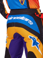Alpinestars 2025 Fluid Wurx Pants, calças de motocross, vista traseira em laranja, azul e roxo, com o logótipo Alpinestars branco no assento e um logótipo Astar azul na perna, construção técnica para condução todo-o-terreno