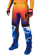 Calças Alpinestars 2025 Fluid Wurx, calças de motocross, gradiente multicolor de laranja, vermelho e roxo com painéis pretos e azuis, usadas com botas azuis e luvas vermelhas, com gráficos do logótipo de estrela e detalhes brancos nos joelhos, equipamento de performance durável para corridas todo-o-terreno