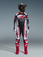 Alpinestars 2026 Techstar Nomur Gear Set, Motocross rider standing in full racing gear, Black white and red design with white speckle pattern, jersey featuring red Astars logo, matching white and red pants, bright red boots, and black helmet with goggles, coordinated high-performance motocross kit