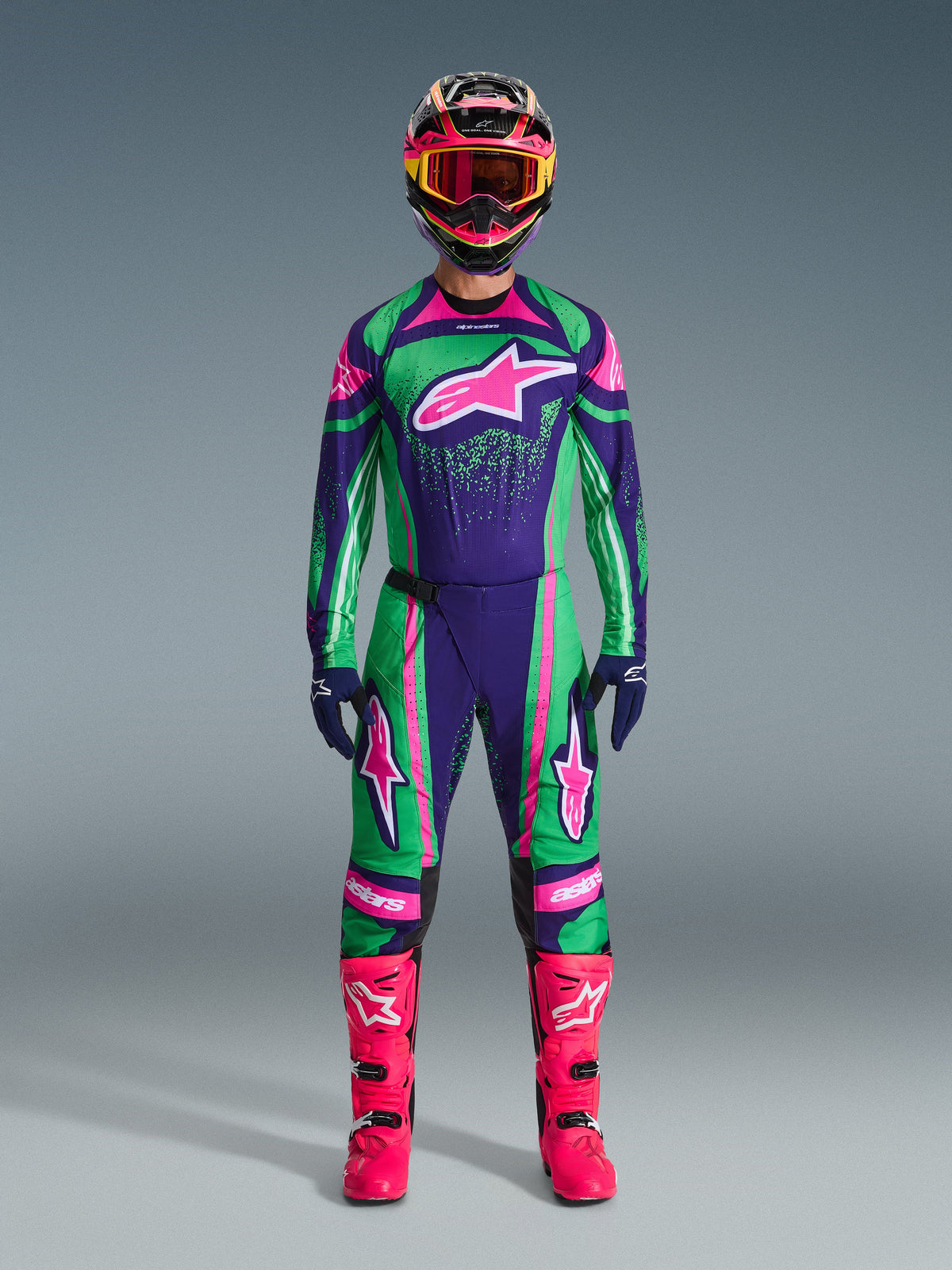 Conjunto de Equipamento Alpinestars 2026 Techstar Nomur, fato de competição de motocross, verde, roxo e rosa vibrantes, logótipo de estrela grande no peito e nas coxas, capacete preto com detalhes rosa e amarelo, botas rosa vivo, design desportivo profissional