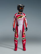 Alpinestars 2026 Techstar Nomur Jersey, Red and White with Black accents and Yellow logos, worn by a motocross rider with matching pants, red boots, and a black helmet, professional off-road racing gear