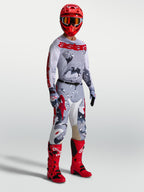 Alpinestars Racer Air Lone, calças de motocross para homem, em camuflado cinzento e vermelho com camisola e botas de moto.