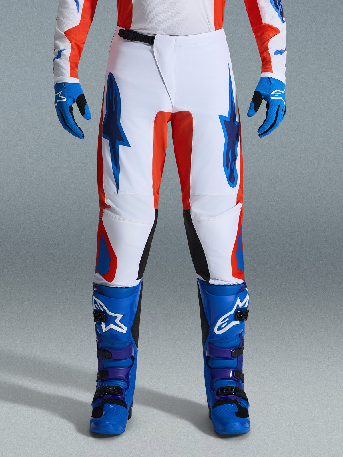 Alpinestars 2026 Fluid Grid Pants, Motocross Pants, Orange and UCLA Blue, worn with matching blue boots and gloves, featuring white chassis with bold blue logos and orange accents, ergonomic design for off-road performance