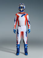 Piloto de motocross com equipamento de corrida completo, calças Alpinestars 2026 Fluid Grid em Laranja e UCLA Blue, camisola branca com mangas laranja e logótipos azuis, capacete e óculos azuis a condizer, botas e luvas azuis, conjunto coordenado para corridas off-road
