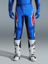 Alpinestars 2026 Fluid Grid Pants, calças de motocross, azuis e vermelhas, com logótipos de estrela vermelhos e brancos em destaque nas coxas, usadas com luvas azuis a condizer e botas off-road brancas, corte atlético com painéis duráveis para competição