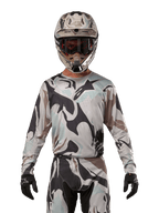 Alpinestars 2024 Racer Tactical Jersey, camisola de motocross, padrão camuflado Iron Camo Dust Gray, piloto a usar capacete e óculos a condizer com luvas pretas, equipamento técnico para corridas fora de estrada