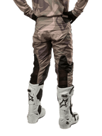 Alpinestars 2024 Racer Tactical Pants, calças de motocross, camuflagem verde militar e castanho, vista traseira mostrando o padrão de camuflagem e painéis elásticos pretos respiráveis na parte inferior das pernas, usadas com botas de motocross brancas, equipamento técnico durável para condução fora de estrada