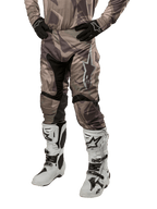 Alpinestars 2024 Racer Tactical Pants, calças de motocross, camuflado verde militar e castanho, usadas com camisola camuflada a condizer, luvas pretas e botas brancas com logótipos de estrela, com painéis elásticos pretos e design ergonómico, conjunto de equipamento todo-o-terreno sobre fundo branco