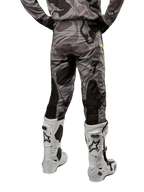 Alpinestars 2024 Racer Tactical Pants, calças de motocross, Cast Gray Camo Magnet, vista traseira que mostra o padrão de camuflagem e zonas elásticas pretas respiráveis, usadas com botas de motocross brancas e pretas, concebidas para condução todo-o-terreno