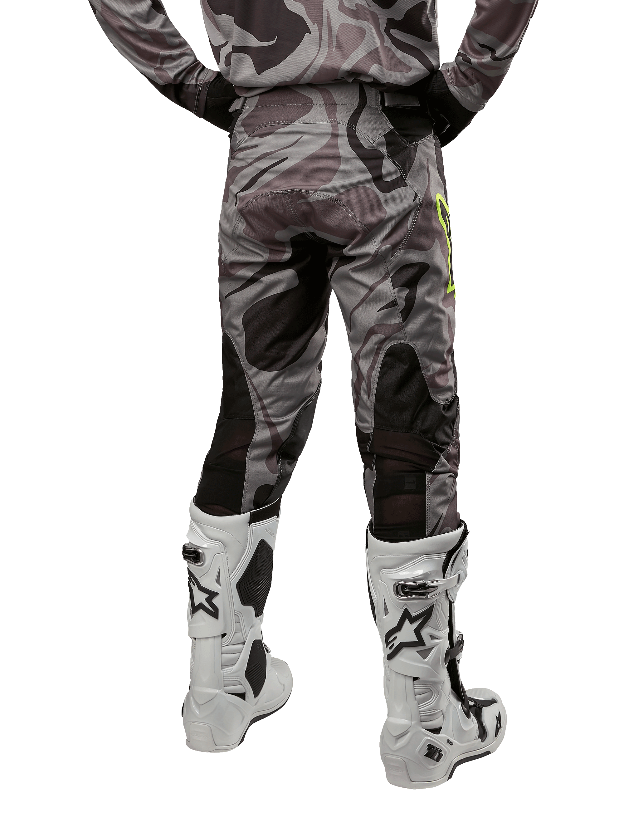Alpinestars 2024 Racer Tactical Pants, calças de motocross, Cast Gray Camo Magnet, vista traseira que mostra o padrão de camuflagem e zonas elásticas pretas respiráveis, usadas com botas de motocross brancas e pretas, concebidas para condução todo-o-terreno