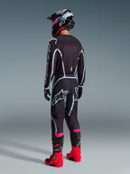 Calças Alpinestars 2026 Fluid Apex, calças de motocross, pretas e cinzentas, vista traseira com logótipo Alpinestars branco no assento, usadas com camisola a condizer, capacete preto e cor-de-rosa, e botas vermelhas brilhantes