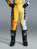 Calças Alpinestars 2026 Fluid Apex, calças de motocross, amarelas e pretas, design de cores divididas com painéis amarelos e brancos, marca vertical 'astars' em destaque, usadas com botas e luvas de motocross pretas, equipamento de performance para condução todo-o-terreno