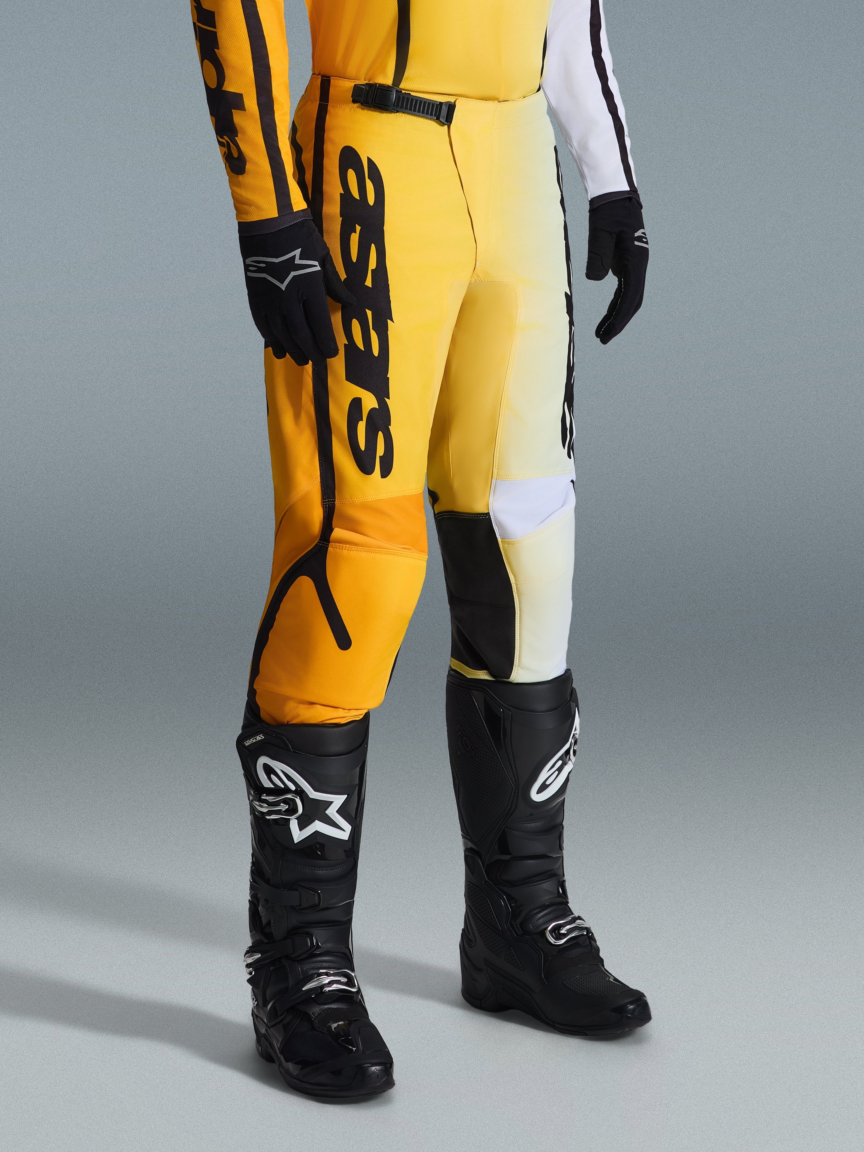 Alpinestars 2026 Fluid Apex Pants, calças de motocross, amarelas e pretas, usadas com botas e luvas pretas, com a marca 'astars' em destaque na coxa, design ergonómico com painéis reforçados, material durável para condução todo-o-terreno