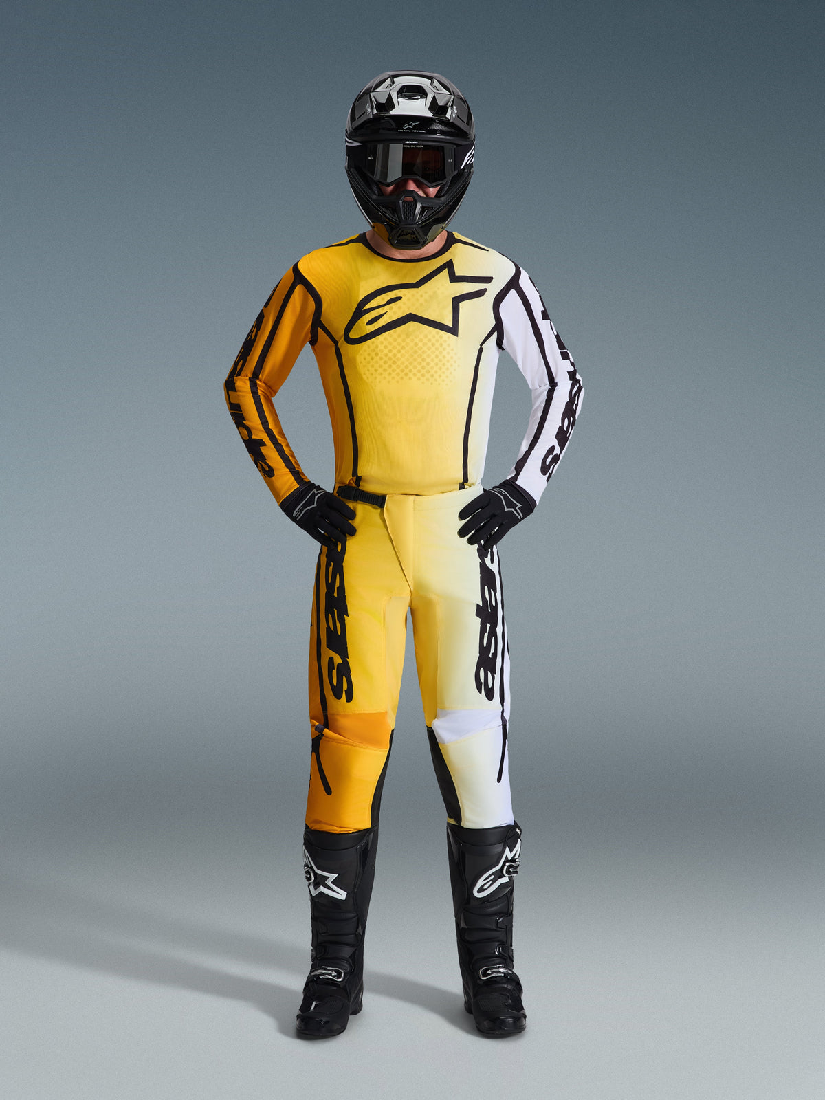 Alpinestars 2026 Fluid Apex Gear Set, equipamento completo de motocross com camisola e calças em gradiente amarelo, laranja e branco, combinado com capacete, óculos e botas pretas, logótipo preto proeminente no peito, proteção completa para corridas todo-o-terreno