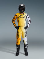 Calças Alpinestars 2026 Fluid Apex, calças de motocross em amarelo, preto e branco, usadas como parte de um kit de corrida completo com camisola em gradiente a condizer, capacete e botas pretos, equipamento profissional de todo-o-terreno
