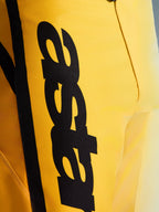 Close-up das calças Alpinestars 2026 Fluid Apex, calças de motocross, amarelas e pretas, com um grande logótipo preto vertical, material durável texturizado e detalhes ergonómicos para desempenho todo-o-terreno