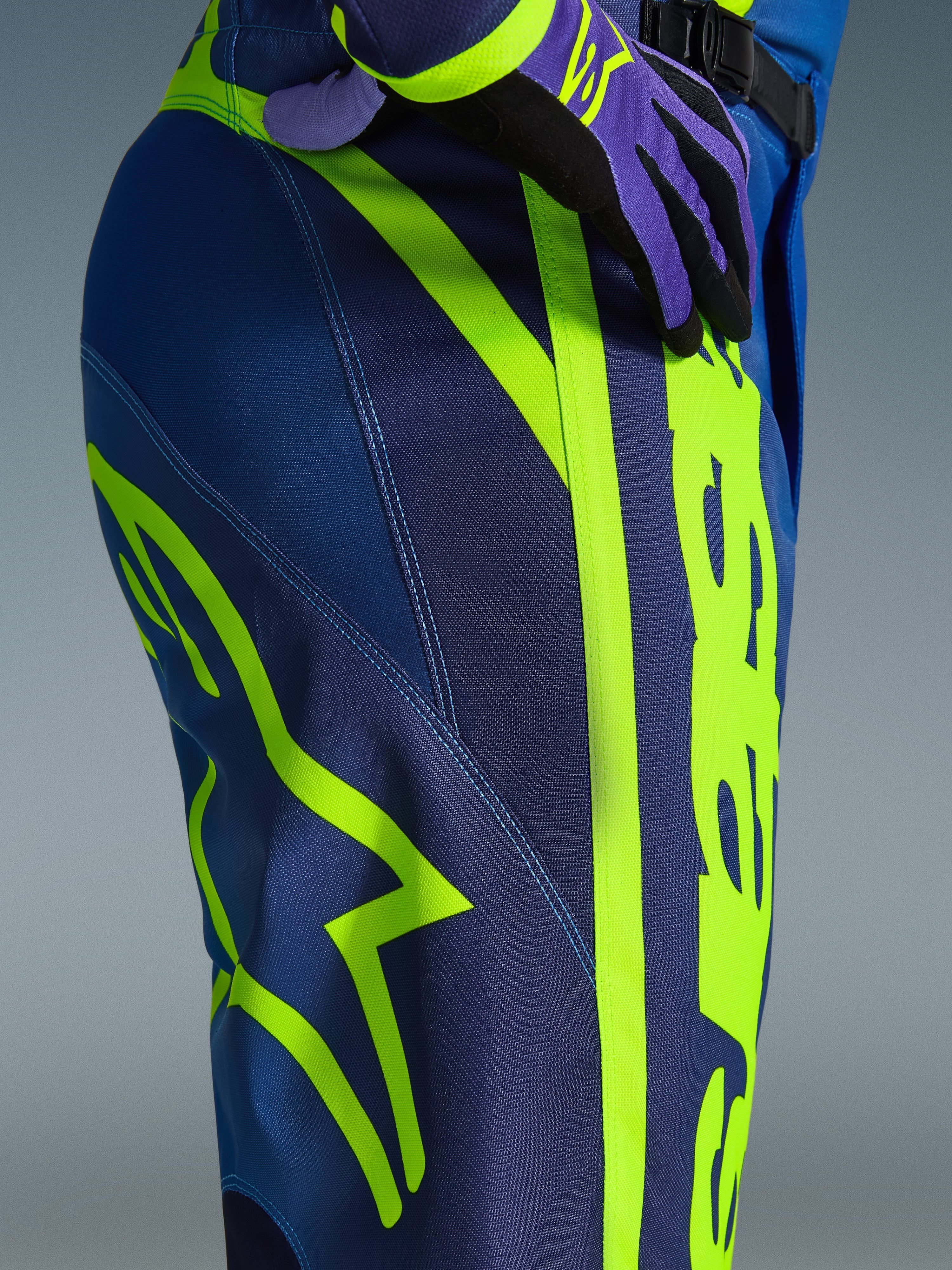 Alpinestars 2026 Fluid Apex Pants, calças de motocross, azul e amarelo fluo, vista aproximada da lateral e anca com branding Alpinestars em amarelo néon, material polifabric durável para condução off-road, parte de um conjunto de equipamento a condizer
