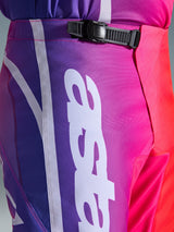 Alpinestars 2026 Fluid Apex Pants, calças de motocross, multicoloridas em roxo, cor-de-rosa e vermelho, grande plano da zona da cintura e anca com um sistema de fecho de catraca preto e grande logótipo Alpinestars vertical em branco, design com gradiente vibrante e textura durável em polifabric