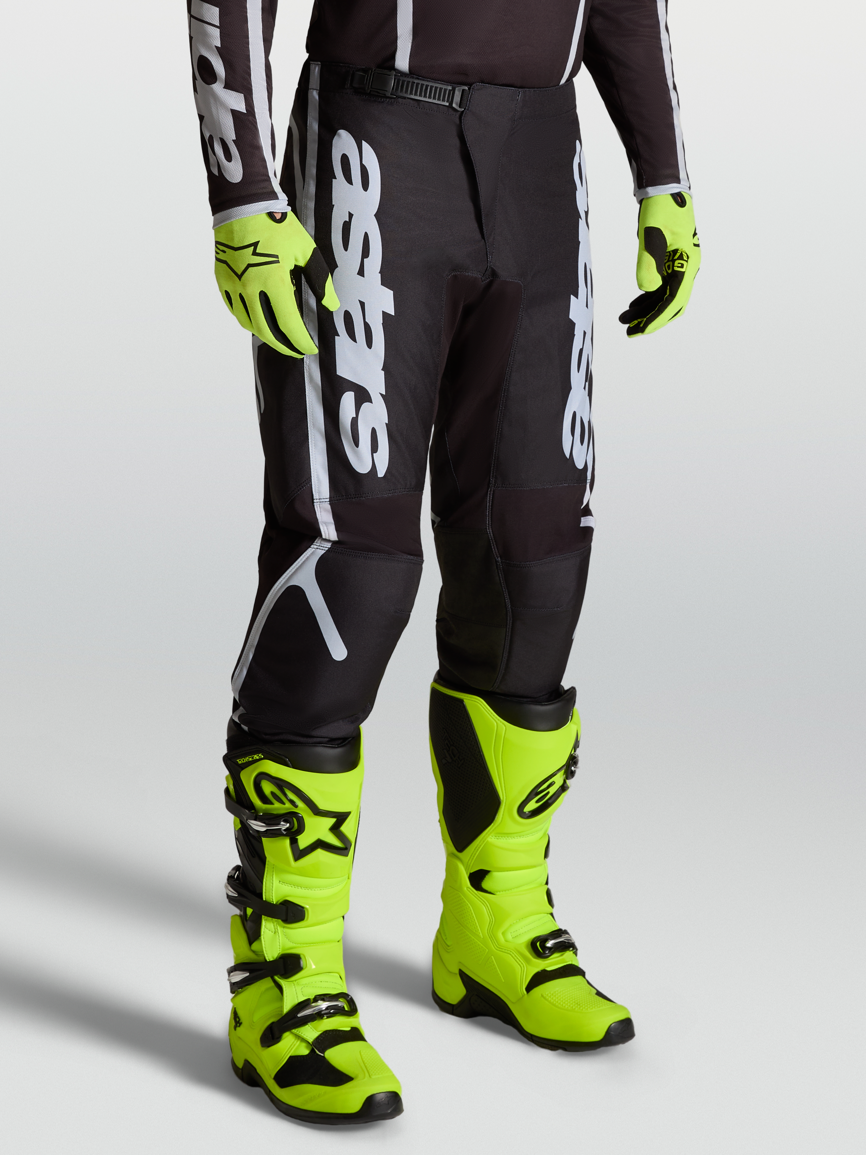 Calças Alpinestars Fluid Apex V2, equipamento de motocross para homem, pretas e prateadas, com botas amarelas vibrantes.