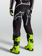 Alpinestars Calças Fluid Apex V2, calças de motocross para homem, preto e prateado, vista traseira e botas amarelo-fluorescentes