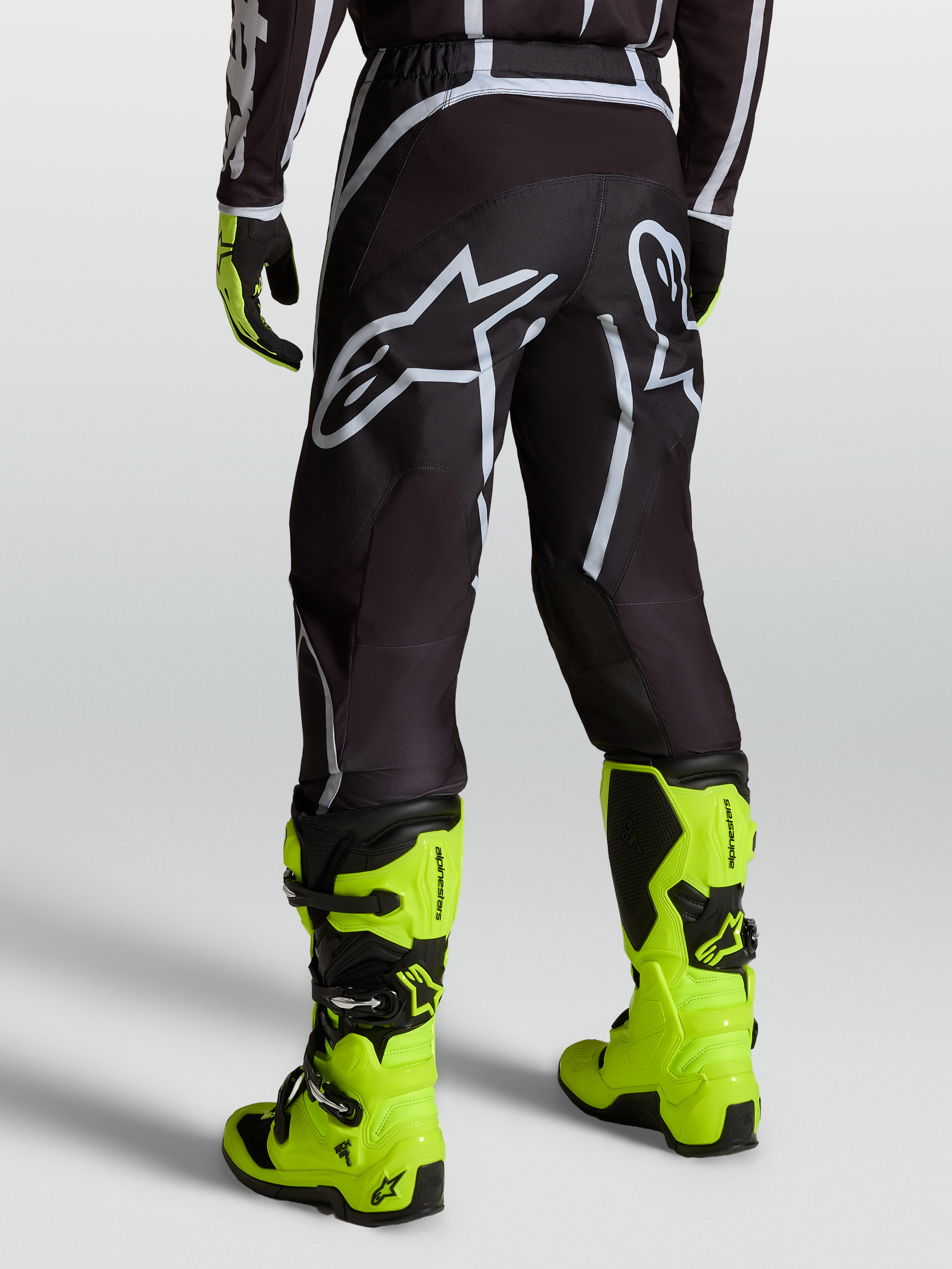 Alpinestars Calças Fluid Apex V2, calças de motocross para homem, preto e prateado, vista traseira e botas amarelo-fluorescentes