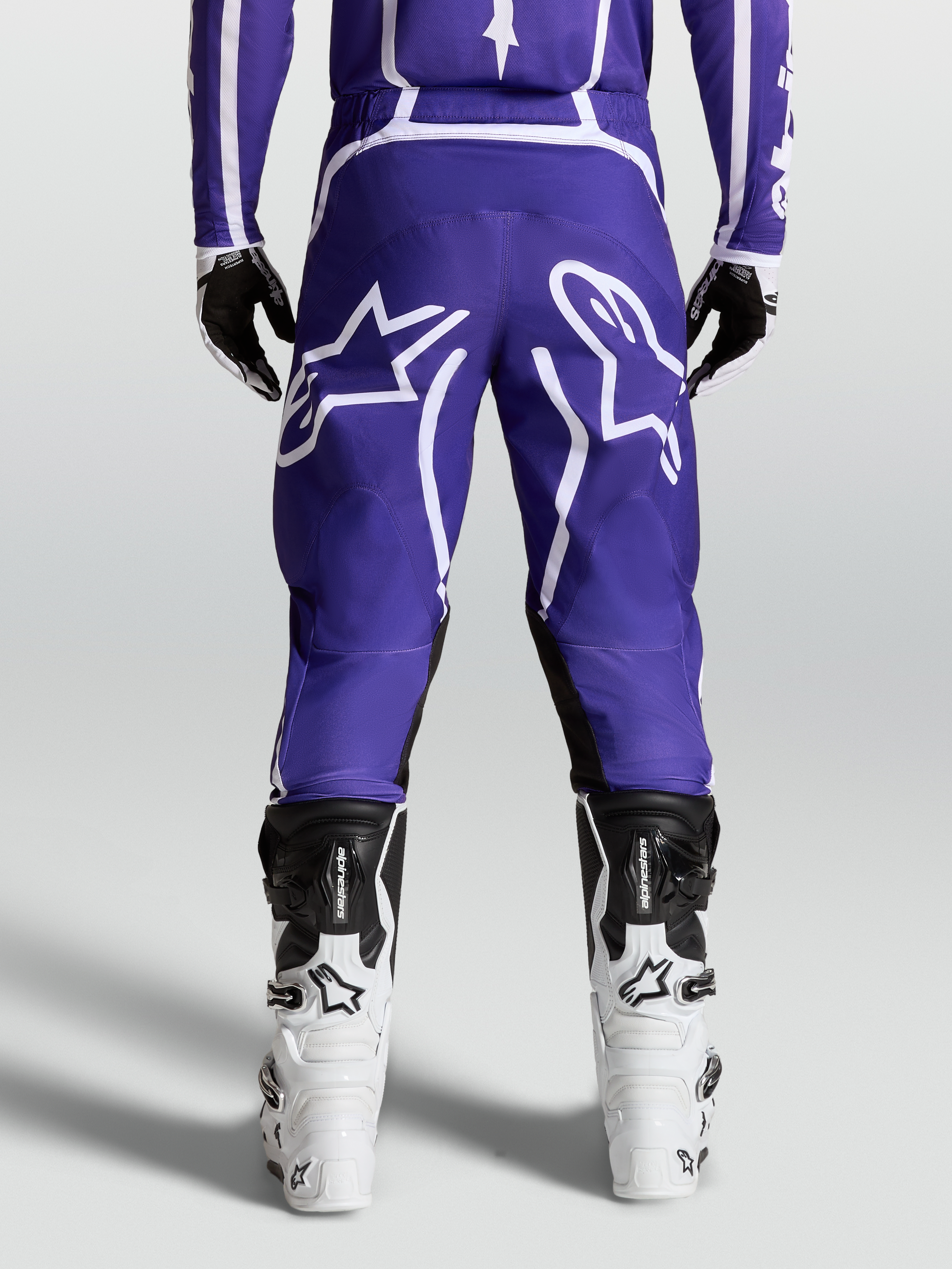 Alpinestars Calças Fluid Apex V2, calças de motocross para homem, azuis e brancas, construção robusta 600D, vista traseira no modelo com botas.