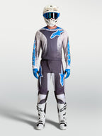 Alpinestars Fluid Drag, calças de motocross para homem, cinzentas e azuis, conjunto completo com camisola e botas brancas.