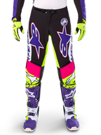 Alpinestars Limited Edition Supertech Dirt Studios Pants, Motocross Pants, White Purple and Yellow Fluo, featuring black panels with neon yellow and pink accents, large purple star logos, shown with matching neon yellow gloves and purple racing boots, durable off-road racing apparel
