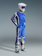 Piloto de motocross a usar as calças Racer Air Portl 2026 em Ucla Blue White, combinadas com uma camisola azul e branca a condizer, capacete branco com óculos azuis e botas brancas, conjunto de equipamento completo para corridas off-road.