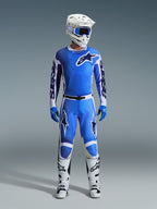 Alpinestars 2026 Racer Air Portl Pants, calças de motocross, azul e branco, usadas como parte de um conjunto completo de equipamento de corrida com camisola a condizer, capacete branco, óculos azuis e botas brancas, apresentando painéis perfurados de elevado fluxo de ar e logótipos destacados para performance em todo-o-terreno.
