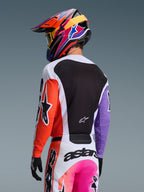 Piloto de motocross visto de costas a usar a camisola Alpinestars 2026 Racer Air Portl em Multicolor, com manga direita laranja, manga esquerda roxa e um grande painel traseiro em malha preta para ventilação, combinada com calças de motocross a condizer e um capacete vibrante e colorido, equipamento profissional de corrida off-road.