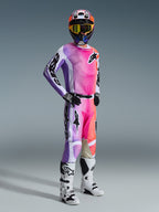 Piloto de motocross com calças Alpinestars 2026 Racer Air Portl em Multicolor, apresentando um design vibrante em degradê rosa, roxo e laranja, combinadas com camisola a condizer, botas de motocross brancas e pretas, e capacete coordenado com óculos amarelos, equipamento completo de corrida para todo-o-terreno