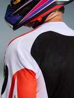 Alpinestars 2026 Racer Air Portl Jersey, camisola de motocross, multicolor com painéis brancos, pretos e vermelhos, primeiro plano da construção em malha perfurada no ombro e nas costas para ventilação, usada com um capacete de motocross colorido