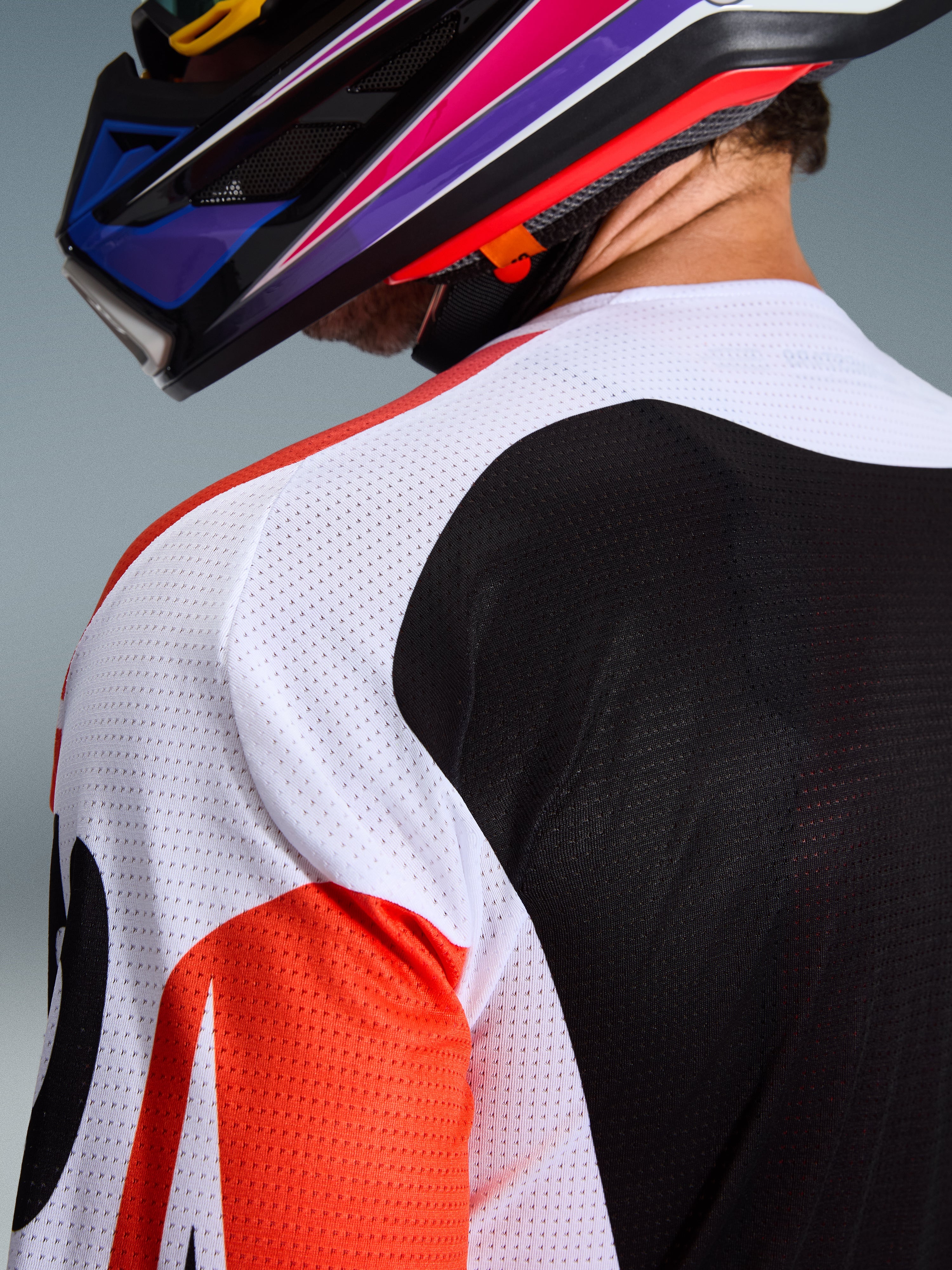 Alpinestars 2026 Racer Air Portl Jersey, camisola de motocross, multicolor com painéis brancos, pretos e vermelhos, primeiro plano da construção em malha perfurada no ombro e nas costas para ventilação, usada com um capacete de motocross colorido