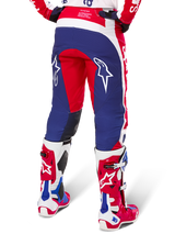 Alpinestars Limited Edition Techstar Fortitude Pants, calças de motocross, vermelhas, brancas e azuis, vista traseira com botas vermelhas e brancas a condizer, logótipos de estrela brancos nas coxas, design durável de múltiplos painéis para competição profissional de todo-o-terreno.