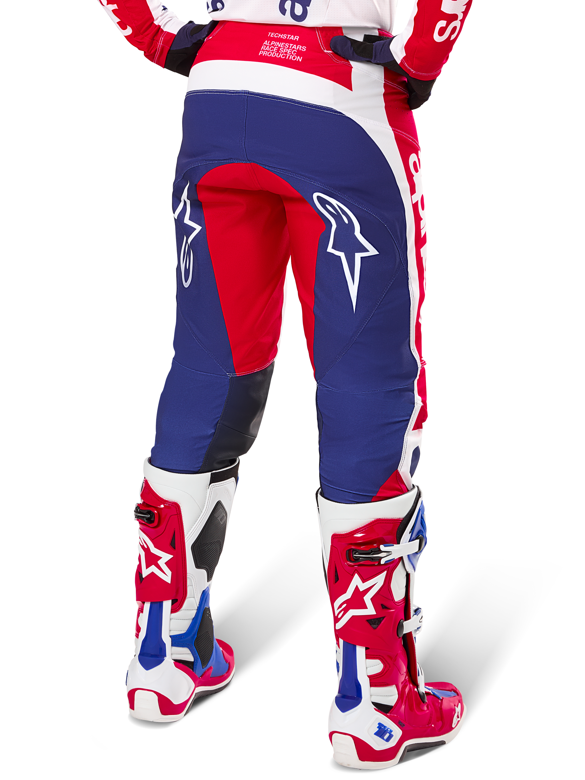 Alpinestars Limited Edition Techstar Fortitude Pants, calças de motocross, vermelhas, brancas e azuis, vista traseira com botas vermelhas e brancas a condizer, logótipos de estrela brancos nas coxas, design durável de múltiplos painéis para competição profissional de todo-o-terreno.