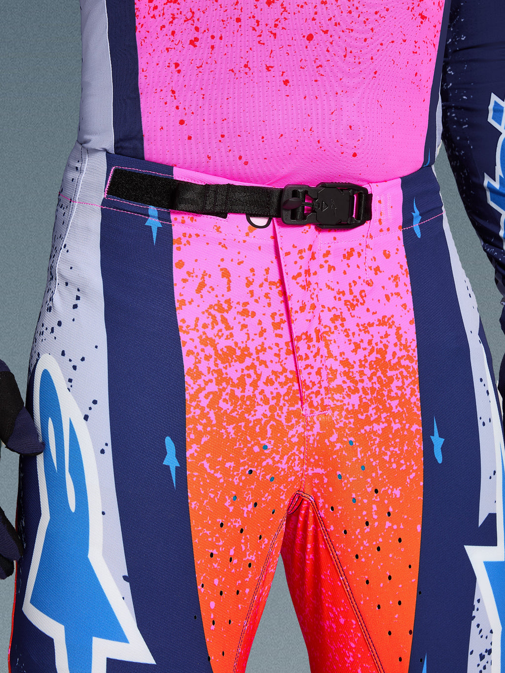 Alpinestars Limited Edition Supertech Records Pants, Motocross Pants, Multicolor pink and orange with navy blue side panels, close-up view of the waist featuring a black SX1 auto-locking magnetic buckle, rip-stop fabric with splatter graphics and laser-cut perforations.