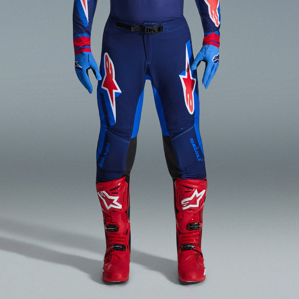 Alpinestars 2026 Supertech Vista Gear Set, Motocross pants in navy and bright blue with red and white logos, paired with light blue gloves and bright red motocross boots, professional racing apparel.