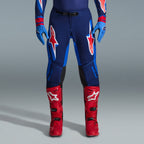 Alpinestars 2026 Supertech Vista Gear Set, Motocross pants in navy and bright blue with red and white logos, paired with light blue gloves and bright red motocross boots, professional racing apparel.