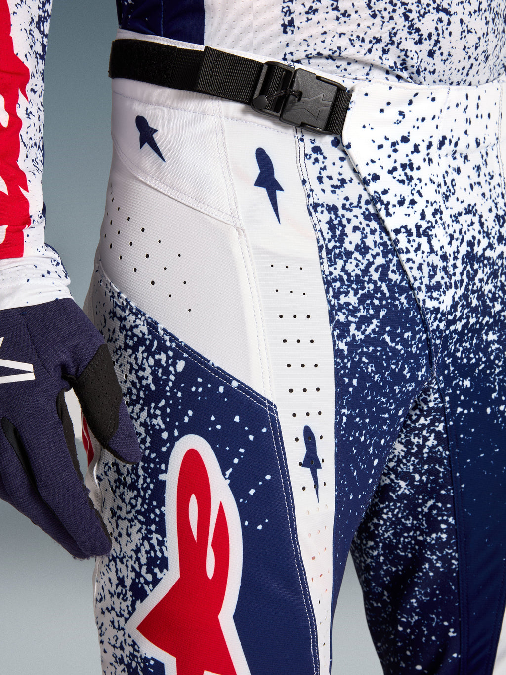 Alpinestars Techstar Unity, calças de motocross, padrão salpicado azul e branco, logótipo vermelho e fivela magnética SX2.